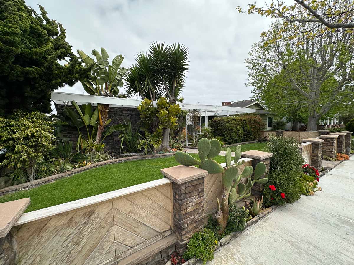 exterior view of home for sale showing angled wood slatted fence, grass and a lot of shrubbery.