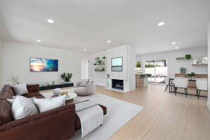 A staged living room with a couch, fireplace, and kitchen/dining area beyond living room.