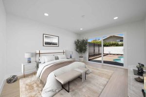 A staged master bedroom showing a bed and nightstands and with a sliding glass door leading to the backyard and pool