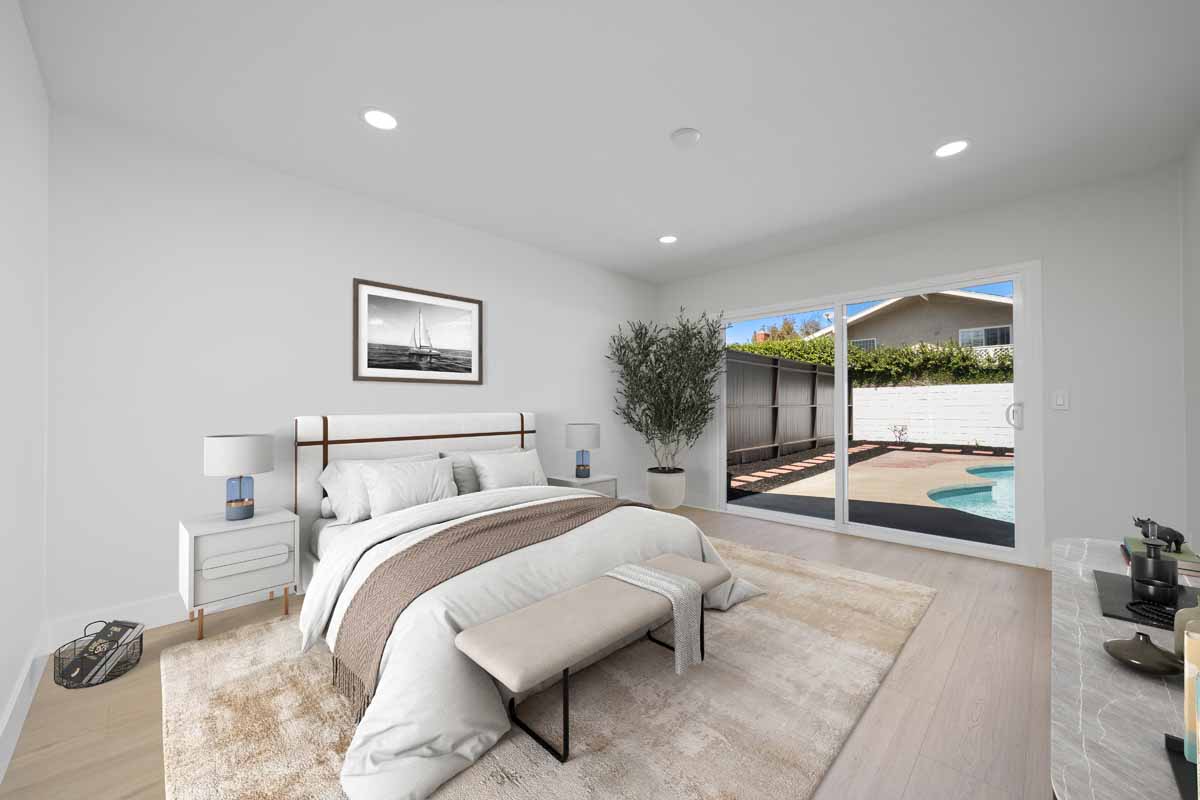 A staged master bedroom showing a bed and nightstands and with a sliding glass door leading to the backyard and pool