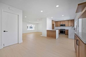 An empty living room adjacent to the kitchen showing neutral colored walls and floor.