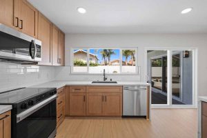 An updated kitchen with light wood cabinetry, white counter tops, and stainless appliances, all looking out through a window to the backyard.