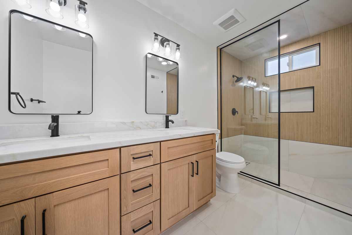 Master bathroom with light wood cabinets and a white counter top, also black fixtures and a large walk-in shower with glass doors.