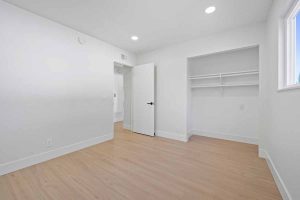 An empty bedroom with neutral colored wood plank floors and a sliding door to a closet.