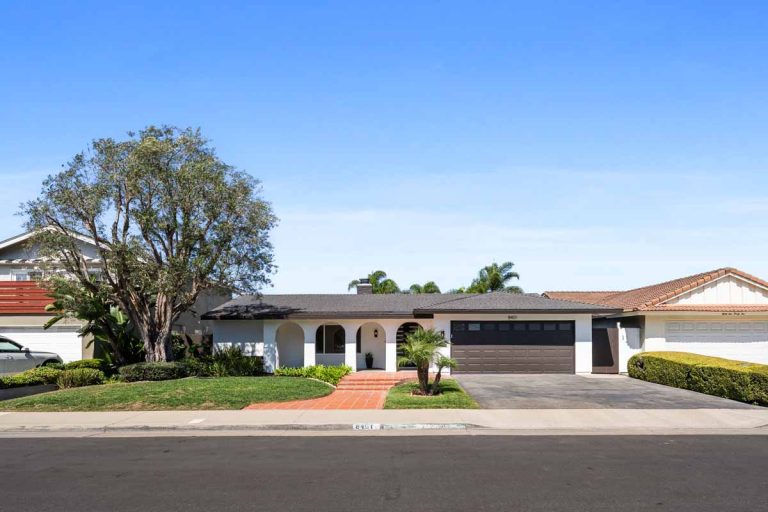 View of home from the street showing white paint, roman arches, a tree and a brown colored garage door.