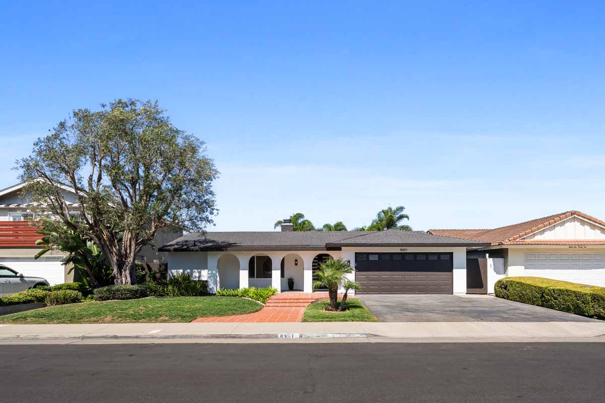 View of home from the street showing white paint, roman arches, a tree and a brown colored garage door.