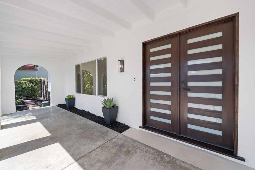 Front exterior view of home with white paint, arches and a vertically lined wooden slatted front door.
