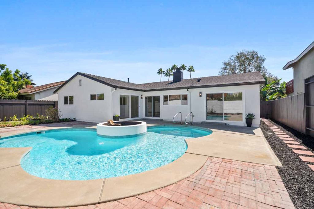 View of backyard and home with white paint showing a pool with a white circular firepit in the center of the pool