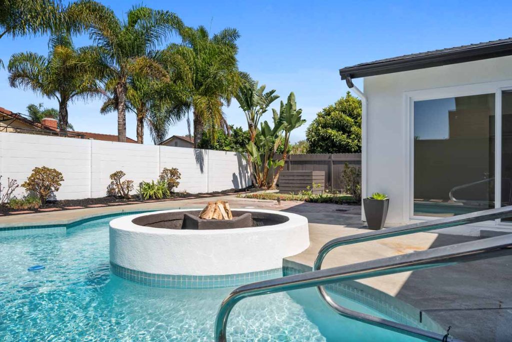 Crystal clear pool with a white circular fire pit within the pool.