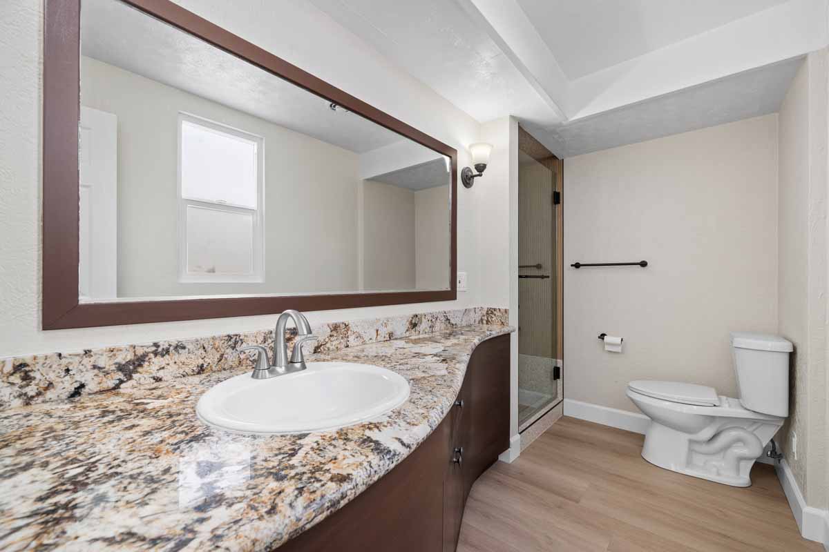 A renovated bathroom showing a long vanity countertop with beige granite, a white sink and silver faucet.