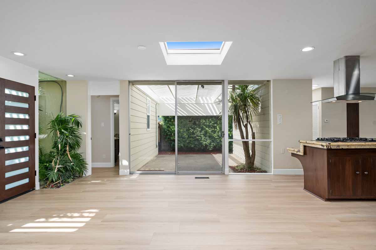 A view of the outside patio through a sliding glass door from inside an updated dining room with light wood flooring.
