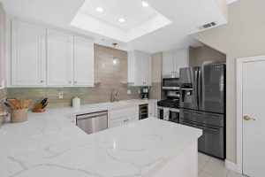 Updated kitchen with white quartz countertops, white cabinets and a tan backsplash.