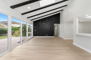 Remodeled dining room with woof tile floors, large windows, and black wood accent wall.