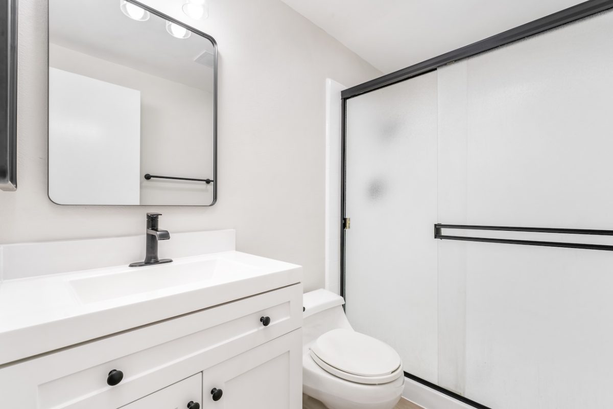 After photo of a bright white bathroom, new counters, toilet, flooring, paint, vanity, and shower. 