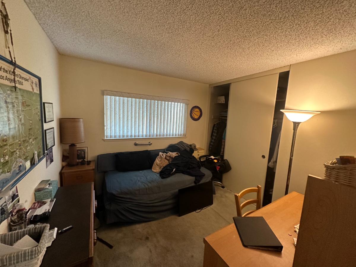Dark bedroom with stained carpet, futon bed, and clutter. 