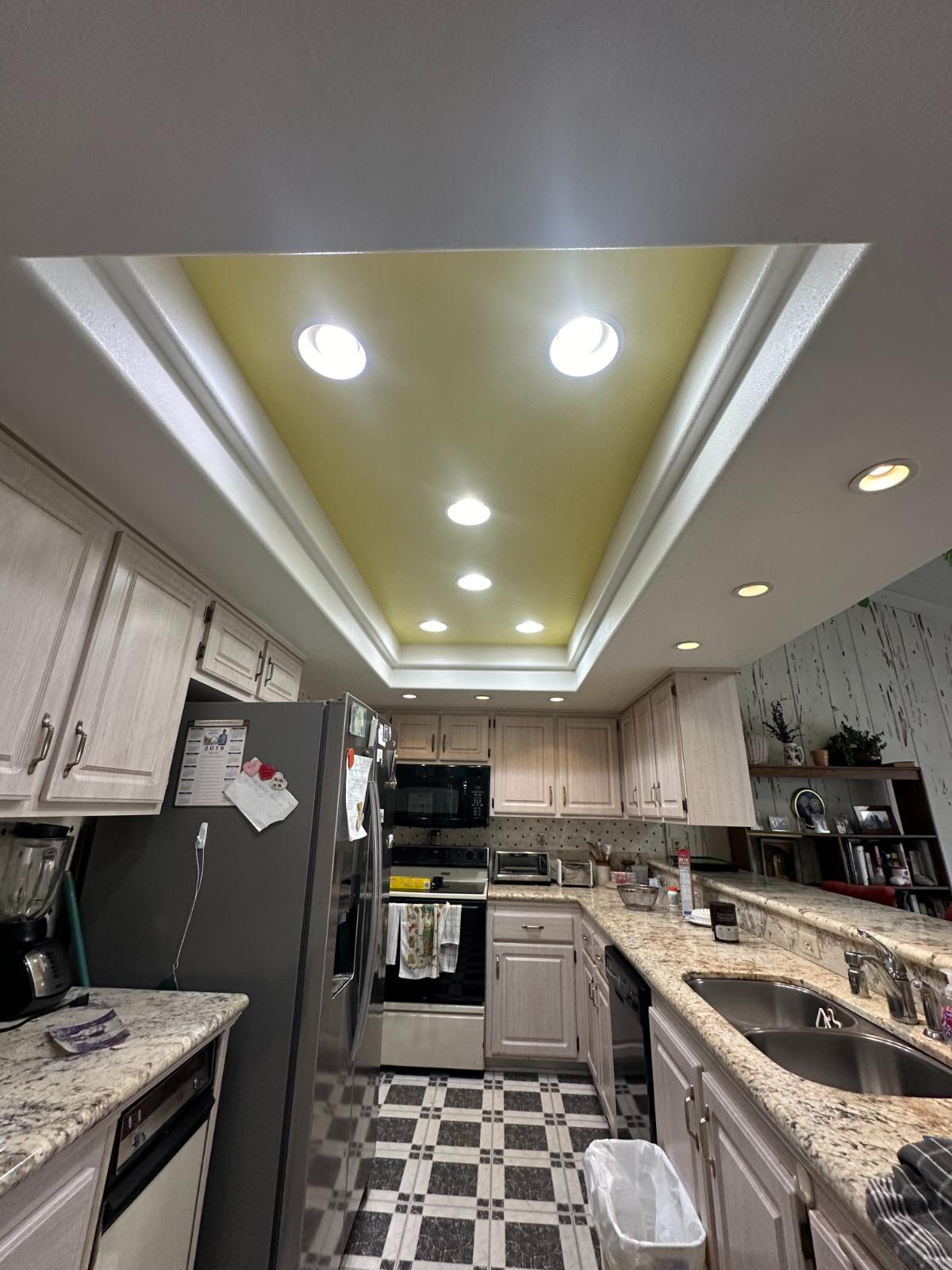 Galley style kitchen with marbled granite countertops, black and white flooring, and recessed lighting panel. 