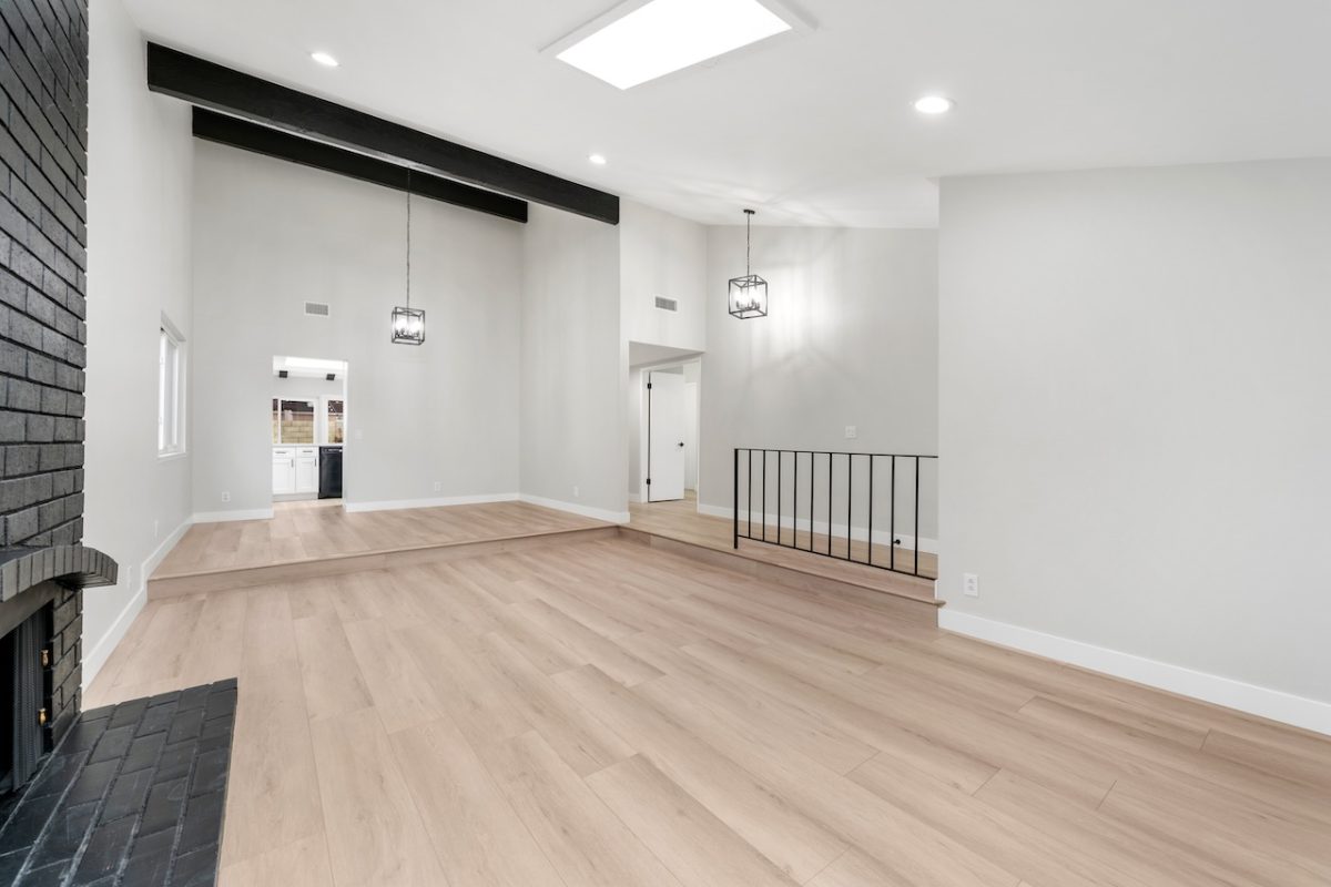 After photo of an open living space with bright white walls, new hardwood flooring, and decorative hardwood beams in the ceiling. 