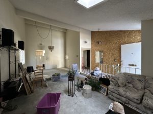 Before photo of a cluttered living space with old carpet, darker walls, and clutter inside.