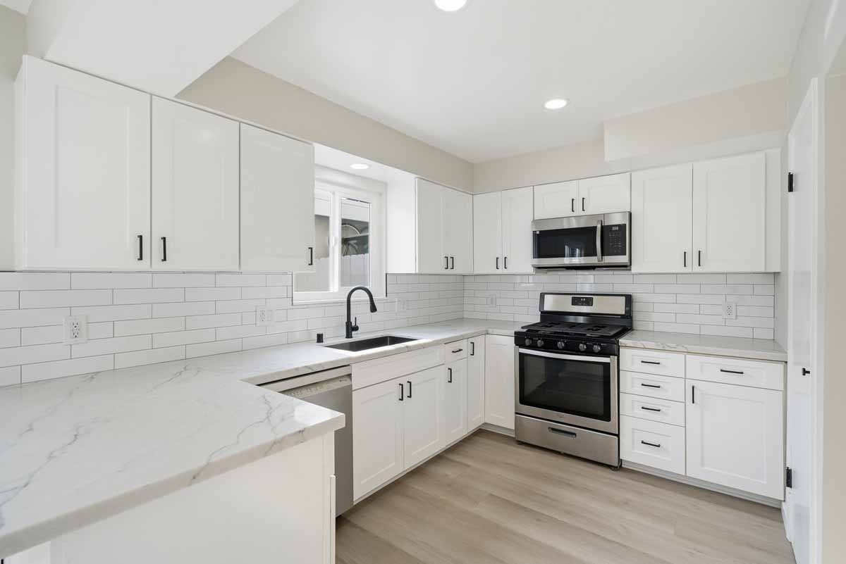 Updated kitchen showing white cabinets, neutral stone counters and stainless and black range.