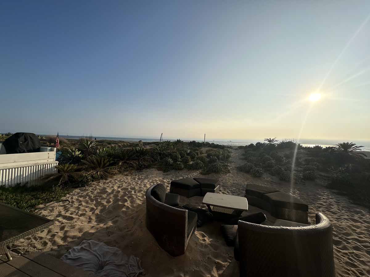 Seating area on the sand with brush and the ocean in the background.
