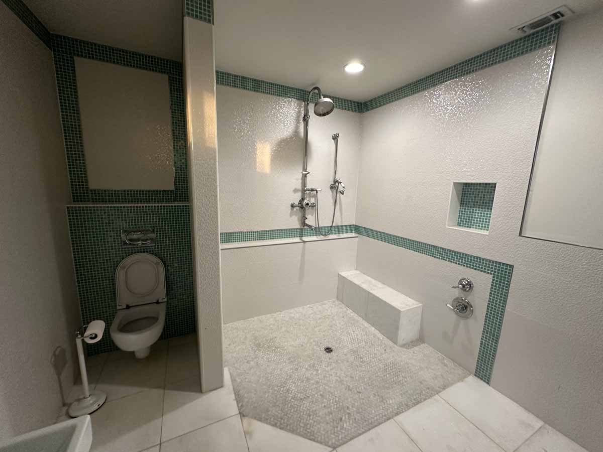 White and teal tiled bathroom with large shower and toilet.