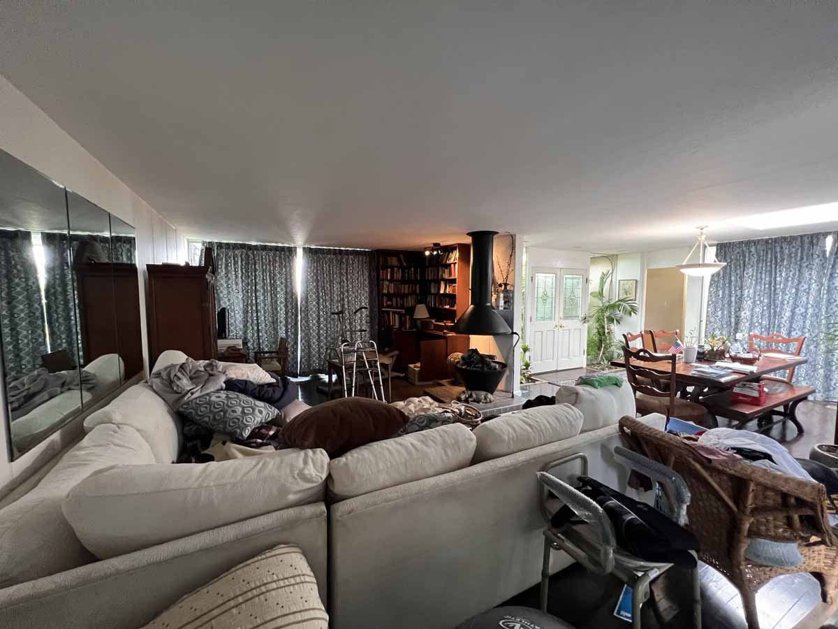 A dark and cluttered living room with a beige couch and dark wood floooring.