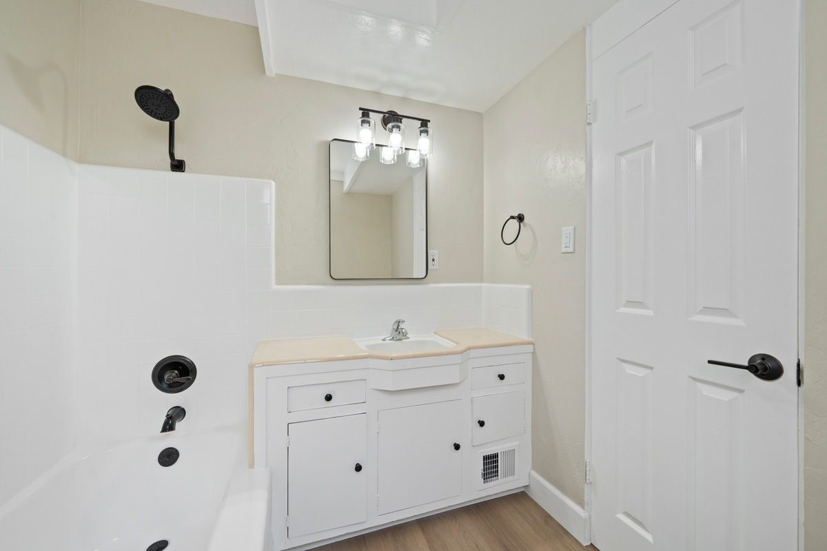 An updated full bathroom with a tub/shower combo, a single sink vanity, all in white an neutral colors with black accent fixtures.