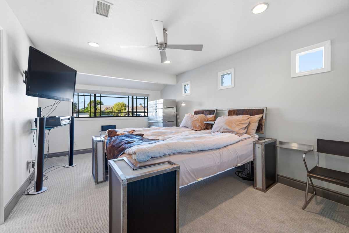 Bedroom with neutral carpet, and walls, a large bed, a mounted television, a ceiling fan, and a window.