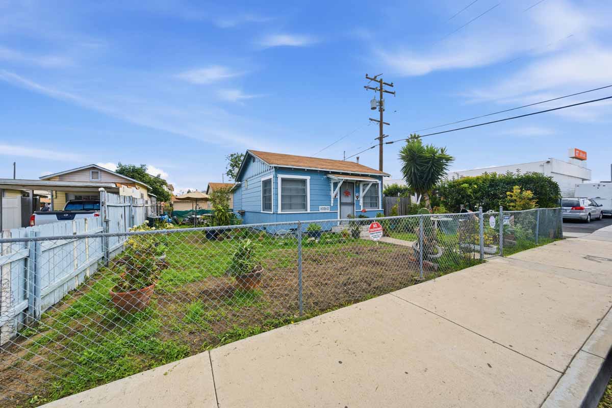 A small blue house behind a chain-link fence.