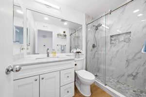Updated bathroom with large white vanity, toilet, and marble-looking walk-in shower with new glass enclosure.