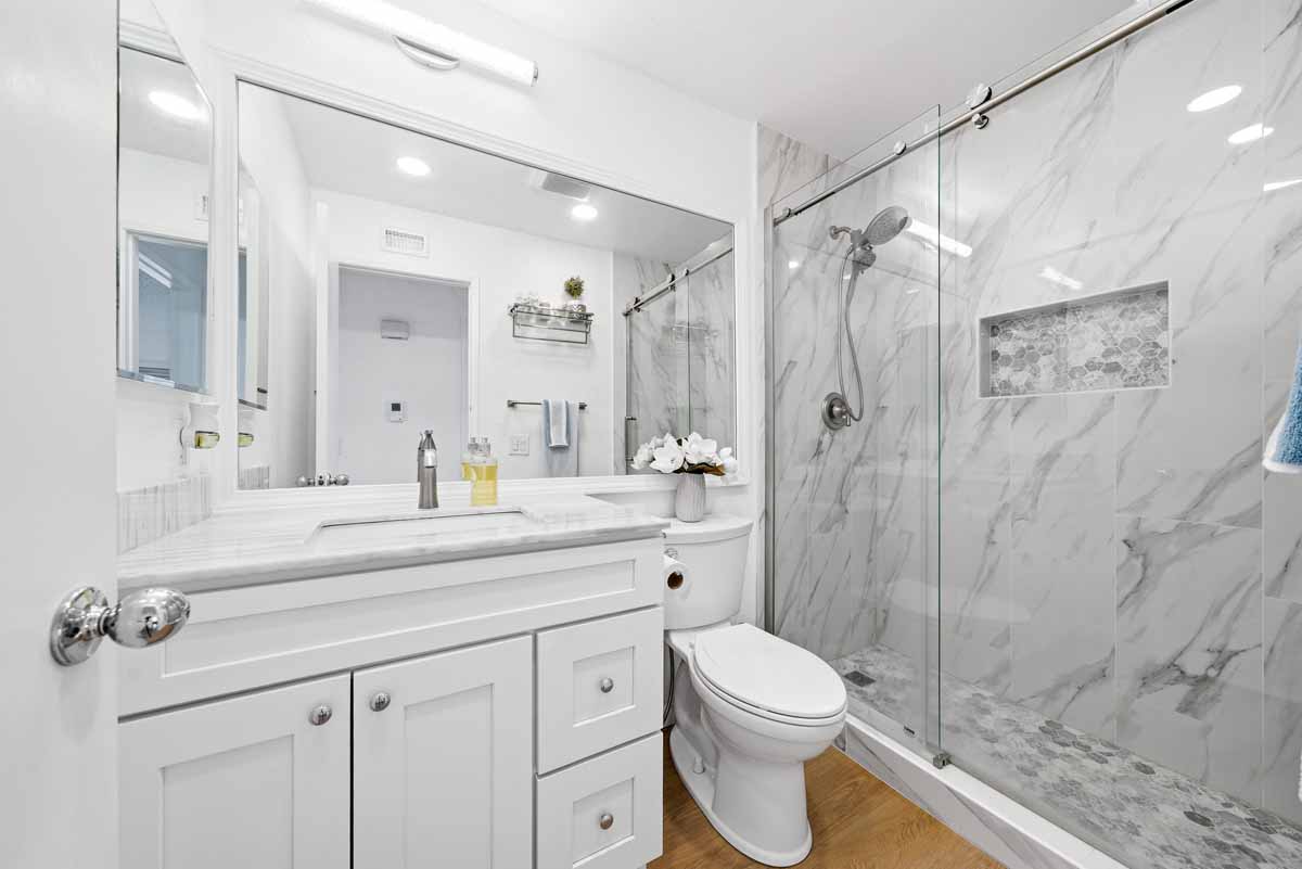 Updated bathroom with large white vanity, toilet, and marble-looking walk-in shower with new glass enclosure.