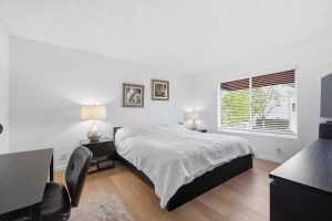 Master bedroom with large bed, two pictures on the wall and a window with wood blinds.