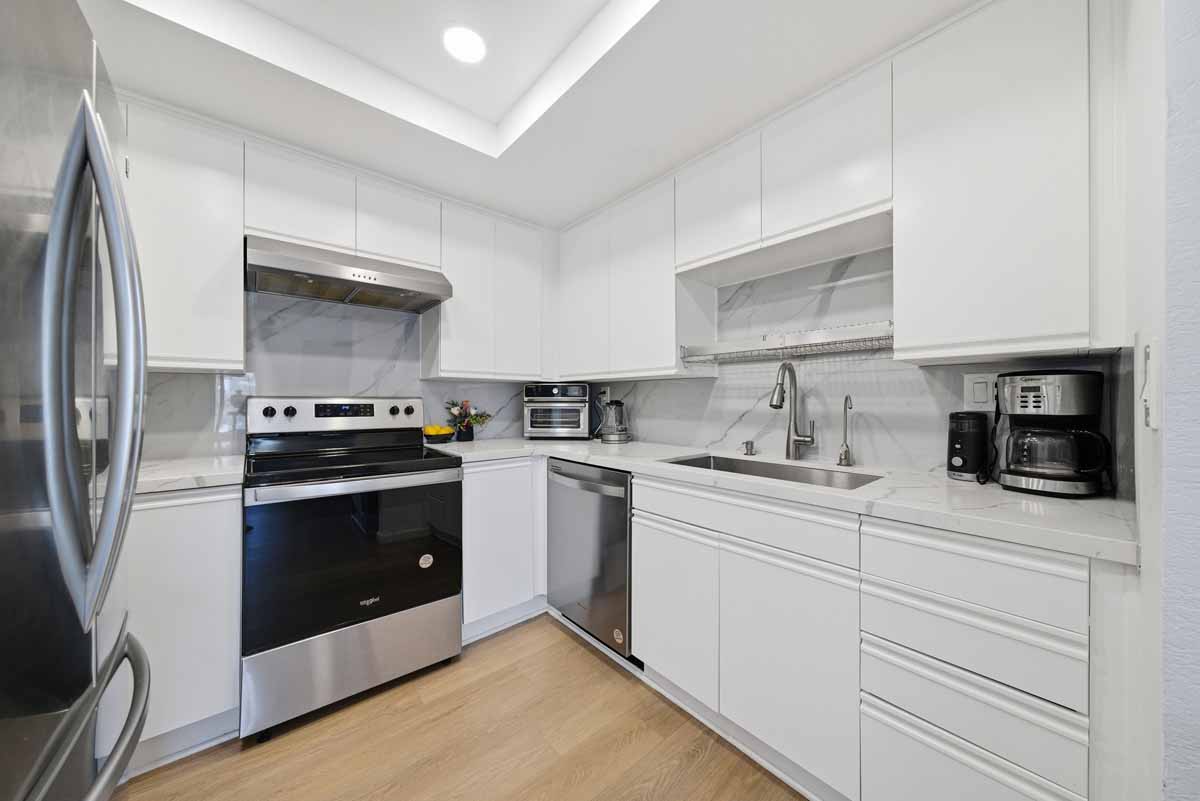 Updated kitchen with white cabinets, a neutral stone counter top, and stainless appliances.