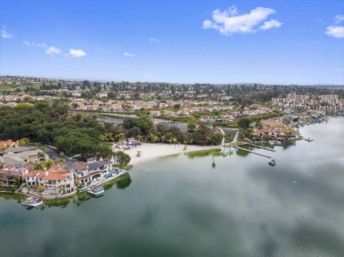 Aerial view of Lake Mission Viejo showing a small beach off the lake with homes and trees surrounding the lake.
