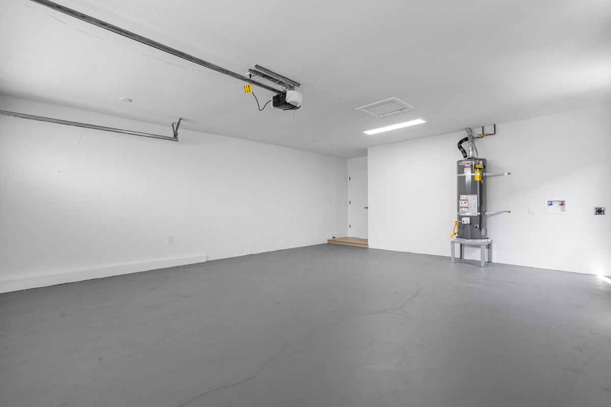 A cleaned and updated garage space showing bright white walls, refinished concrete flooring and a water heater.