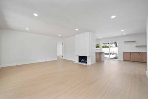 An updated living space showing light colored wood flooring, white walls and a white fireplace.
