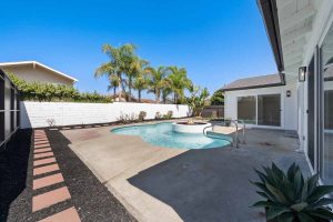 A clean and refreshed backyard pool with a white stuccoed fire pit right off the pool.