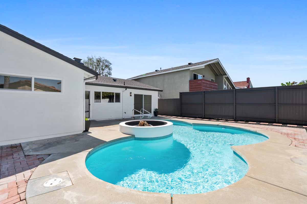 A clean and refreshed backyard pool with a white stuccoed fire pit right off the pool.