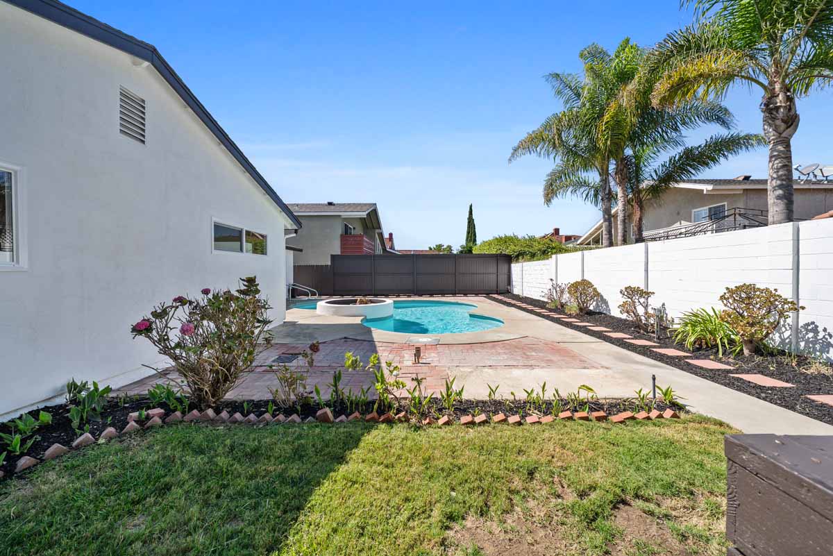 A cleaned up backyard with a bright blue pool, cement and grassy area with a planter full of plants.