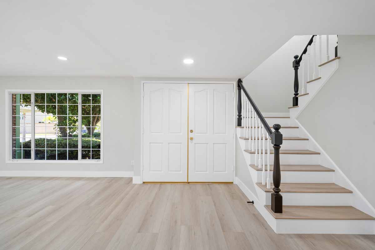 Updated entryway showing light colored flooring and walls, double front doors and a staircase to the right.