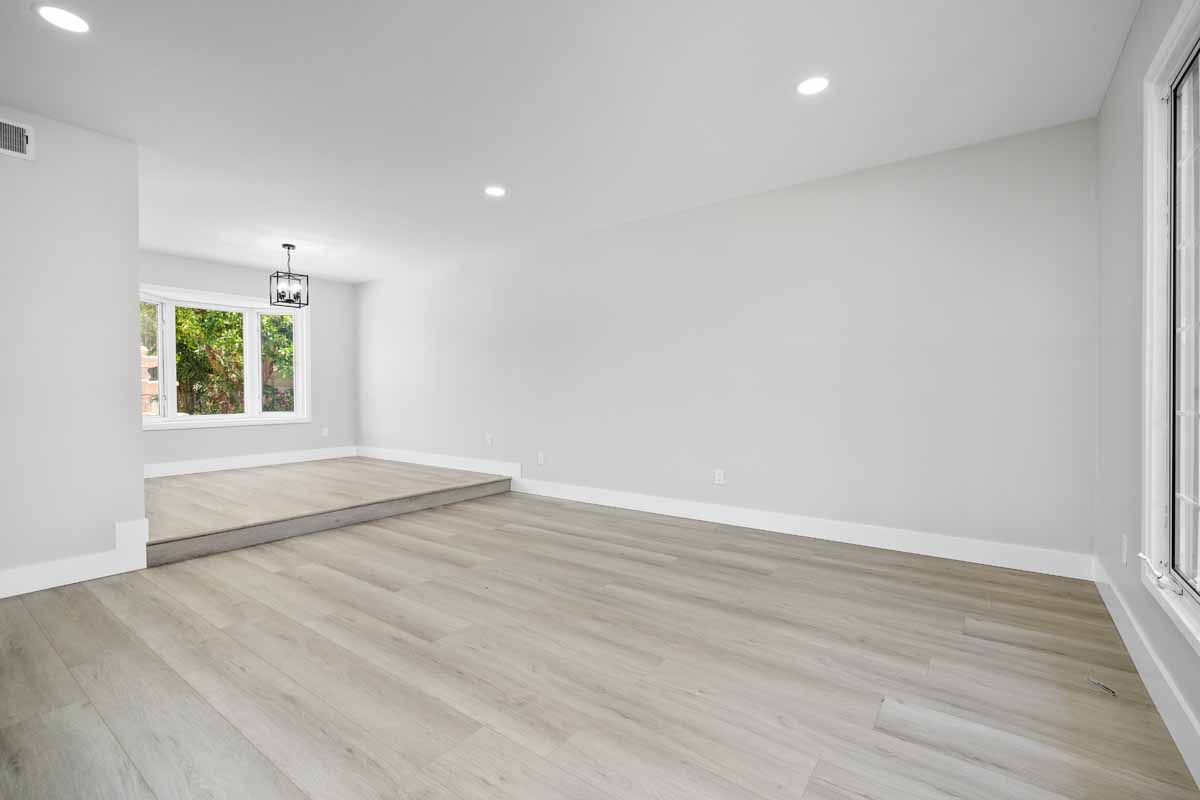 Updated front family room showing light colored wood flooring, light paint on walls, recessed lights and a window looking out towards the backyard.