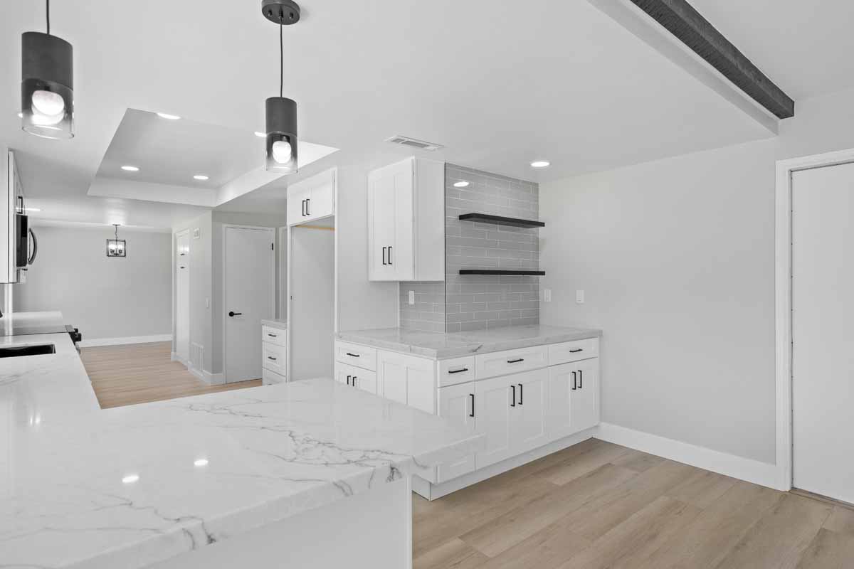 Updated kitchen with light wood colored flooring, neutral paint on walls, white cabinets and stone counters.
