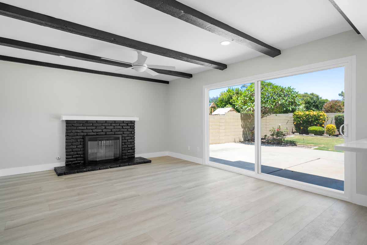 Updated living room with light flooring and walls, dark wood beams on ceiling, and a black painted fireplace.