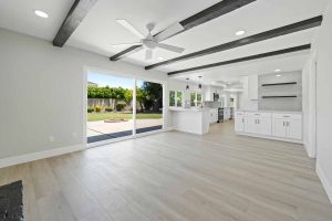 Updated kitchen with light wood colored flooring, neutral paint on walls, white cabinets and stone counters, with a ceiling fan and glass slider leading to backyard.
