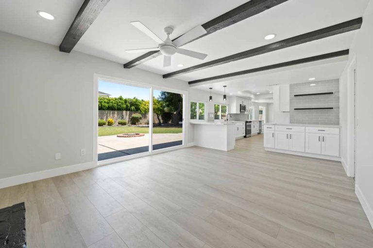 Updated kitchen with light wood colored flooring, neutral paint on walls, white cabinets and stone counters, with a ceiling fan and glass slider leading to backyard.