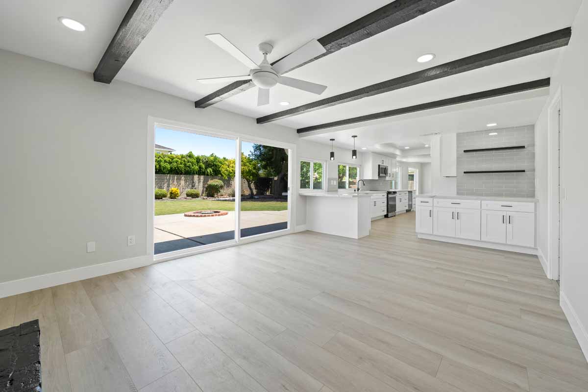 Updated kitchen with light wood colored flooring, neutral paint on walls, white cabinets and stone counters, with a ceiling fan and glass slider leading to backyard.