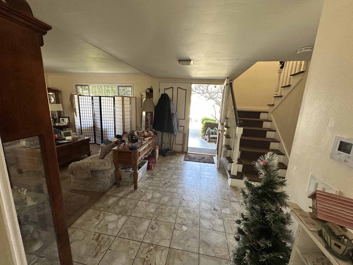 Outdated first floor of home with tile and brown carpet showing a staircase lined with brown carpet.
