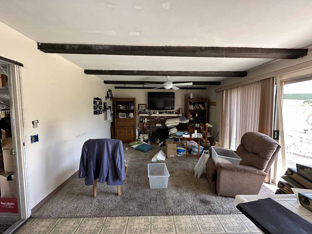 Outdated living room with brown carpet and wood beams on ceiling.