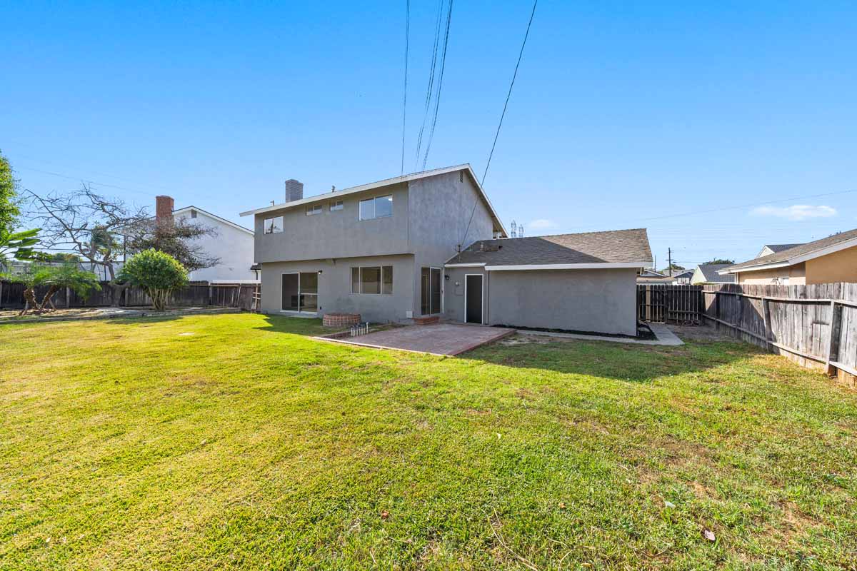 A large grassy space in the backyard showing the gray painted house in the background.