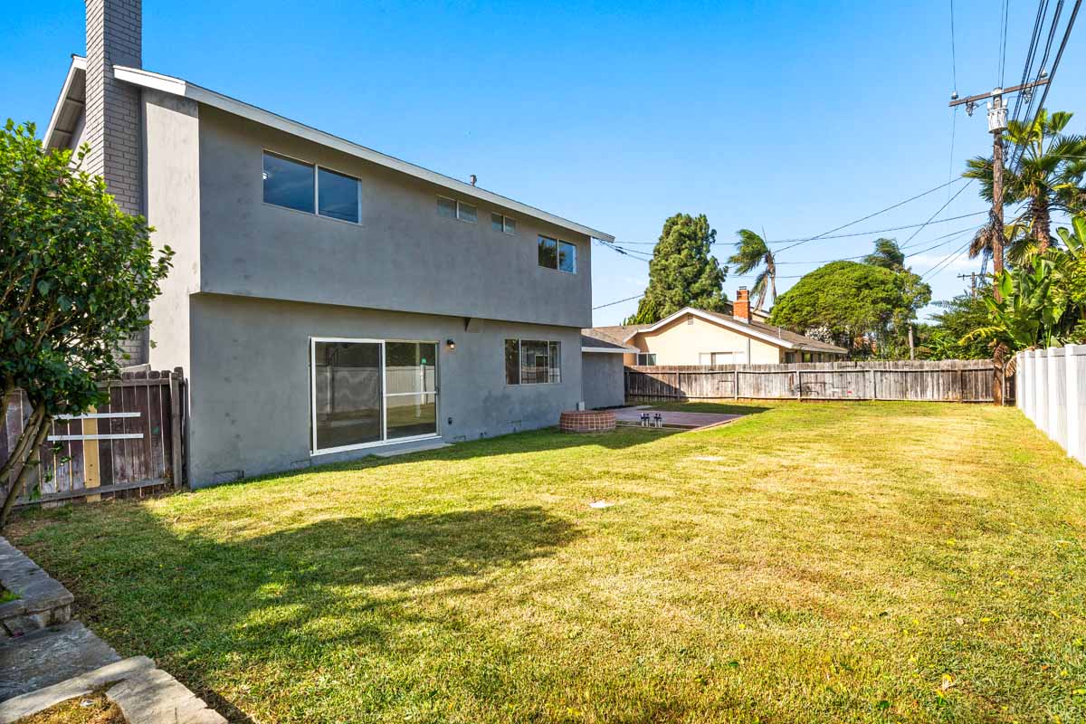A large grassy space in the backyard showing the gray painted house in the background.